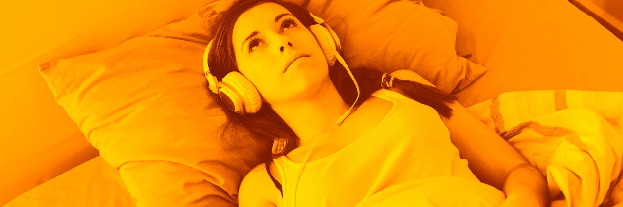 Depression Is Like a Song Stuck in My Head Young Woman Listening Music with Headphones on the Bed. She is Alone, wearing a white Undershirt. The bed has green and orange Sheets. She is Lying down, Looking at Ceiling with a Sad Expression.