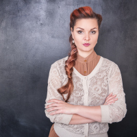 woman with long hair in a braid standing against a wall with her arms crossed