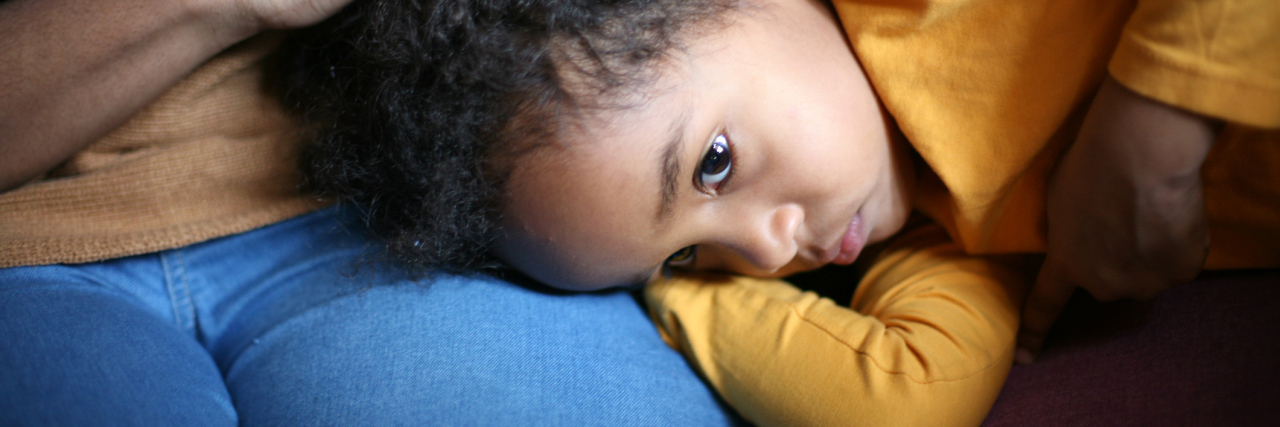 A sad little girl resting her head on her mother's lap.