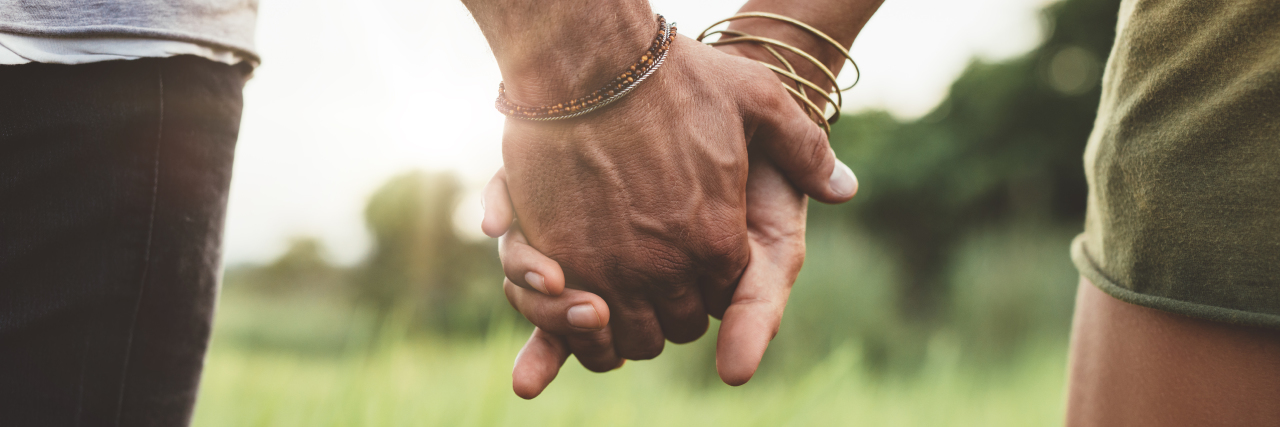 Male and female couple holding hands in a field.