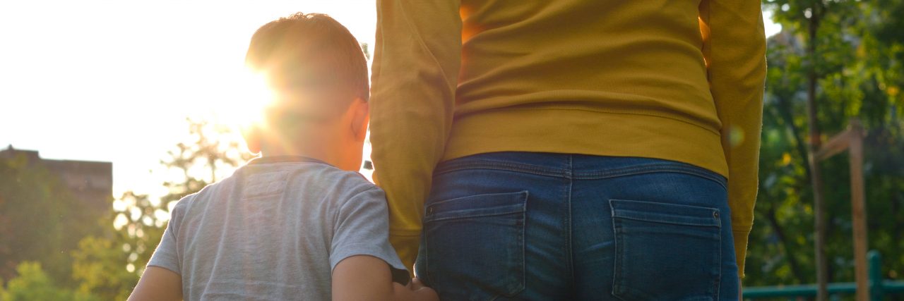 Child holding hands with her parent in nature at sunset.