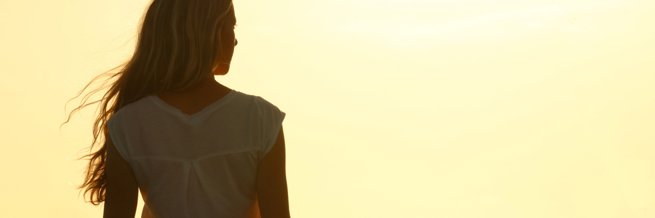 young woman watching sunset silhouette from behind
