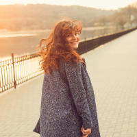 woman walking down a street by a lake and looking over her shoulder to smile
