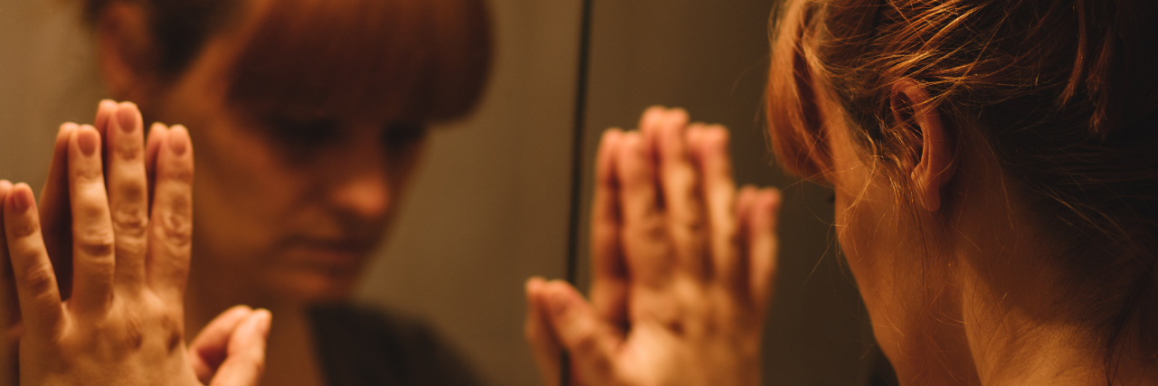 When Symptoms Reappear After a Period of Remission From Illness woman with her hands against the mirror looking at her reflection