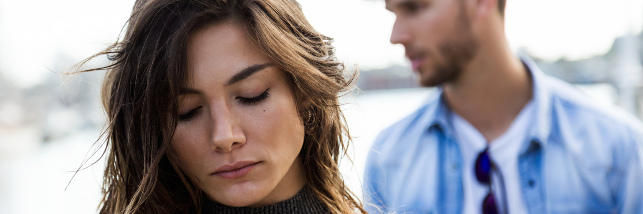 When Do I Disclose My Chronic Illnesses to the Person I'm Dating? The camera focusing on a woman, with a man blurred in the background.