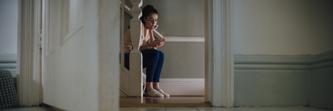 A teenage girl sitting on a staircase looking at her phone.