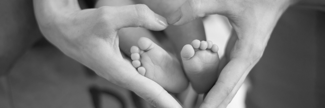 a mother's hands shaped in a heart over her child's feet. black and white.