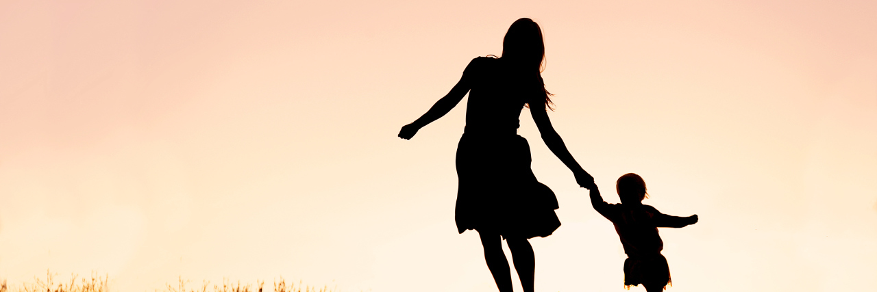 What Its Like to Parent a Child With Batten Disease Silhouette of a happy mother and her baby daughter holding hands, and running and dancing outside at sunset.