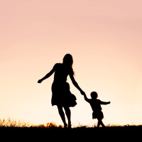 Silhouette of a happy mother and her baby daughter holding hands, and running and dancing outside at sunset.
