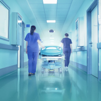 Two nurses wheeling a hospital bed down a hallway.