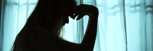 silhouetted woman sitting on bed by window depression