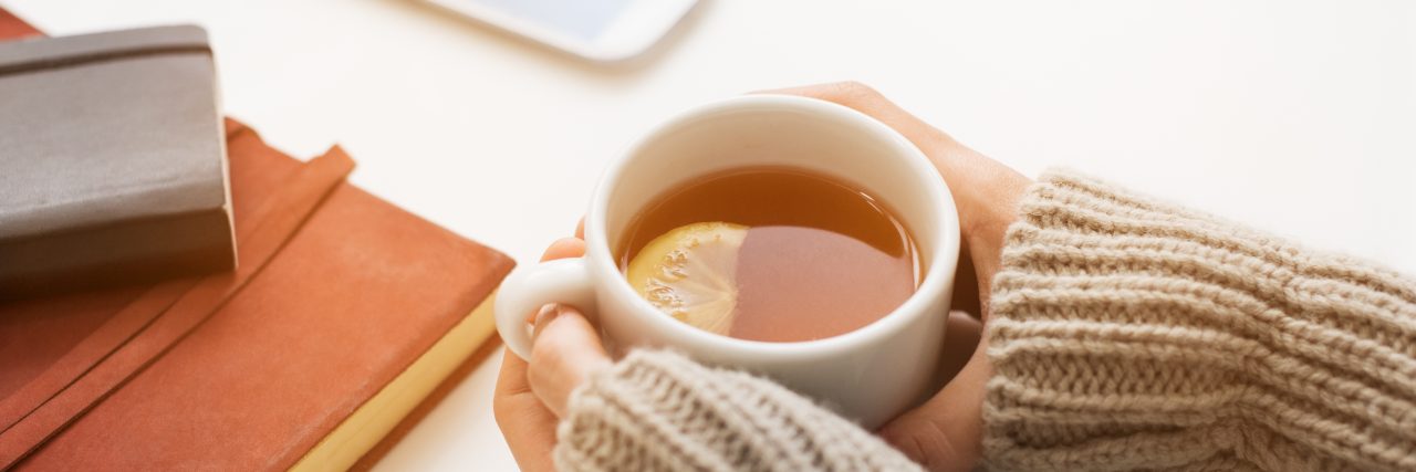 Close up of woman hands holding a cup of lemon tea on white table in a winter afternoon. Woman