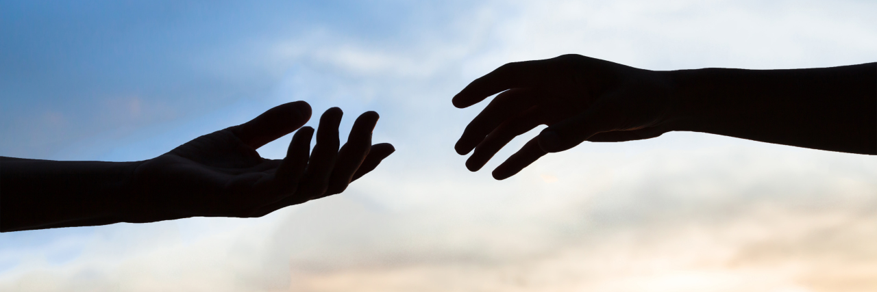 Two hands reaching to help each other, silhouette on sky background.