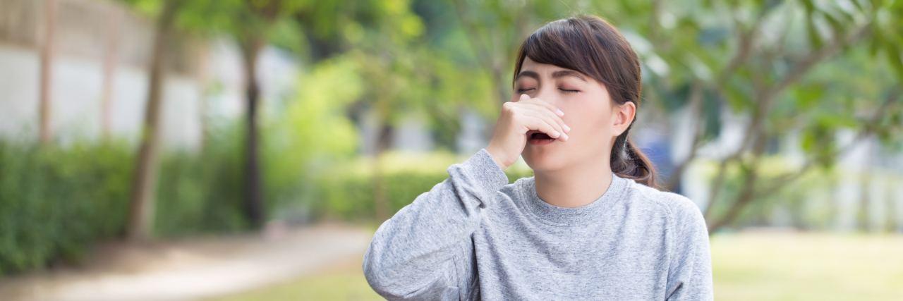 The Unusual Symptoms I Experience With Chiari Malformation woman sitting on a park bench about to sneeze