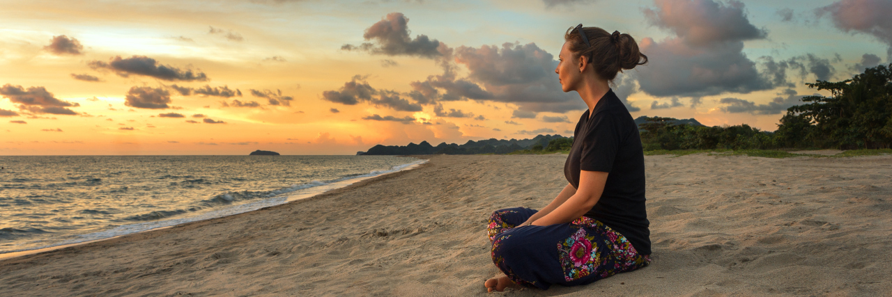 Woman sitting on beach sand and relaxing at sunset.