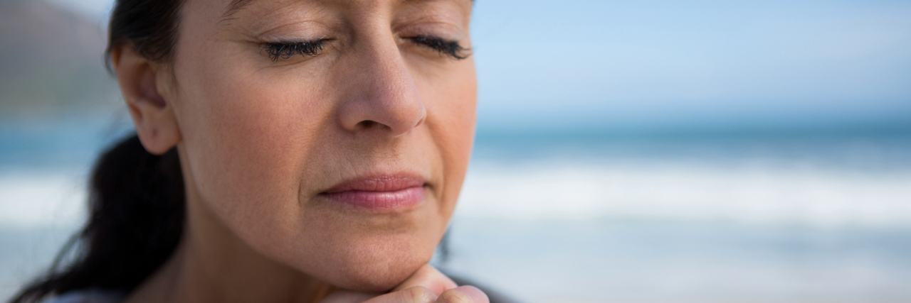 Mature woman praying with hands clasped on beach