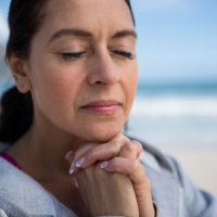 Mature woman praying with hands clasped on beach