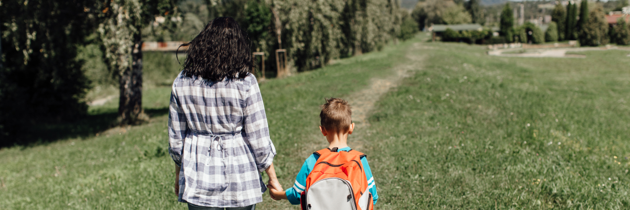 Mother and son walking through grassy field.