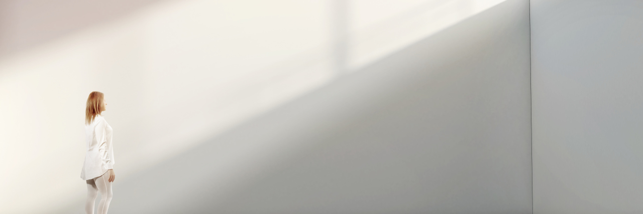 Am I Disabled? Woman walking near blank white wall with sunlight streaming in.