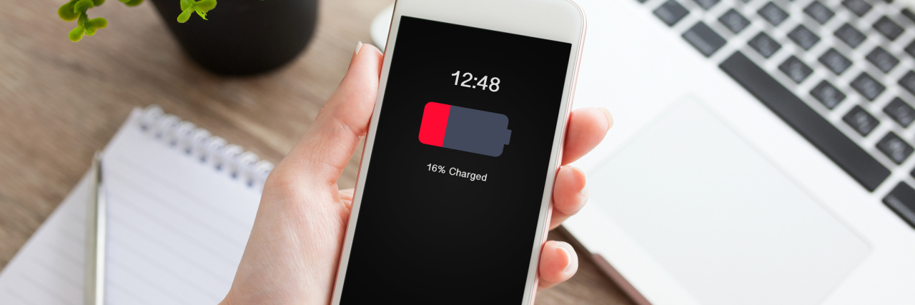 My Depression Is Like a Phone Battery That Drains Faster Than It Shoul female hand holding white phone with low charged battery screen on table laptop