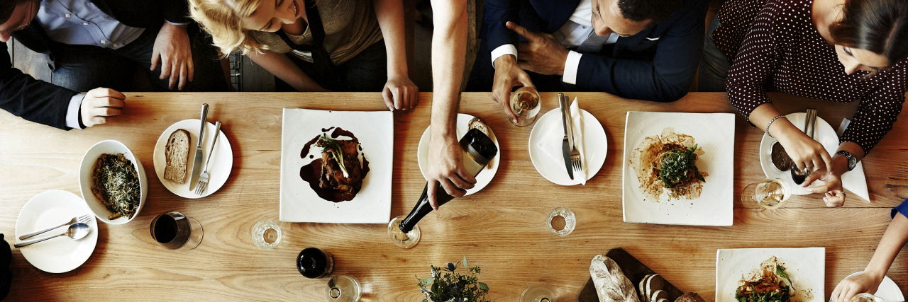 Why Eating Out Causes Me to Experience Anxiety A photo of a table surrounded by people, and plates of food on top of it.