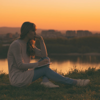 sad woman sitting outside at sunset thinking and writing