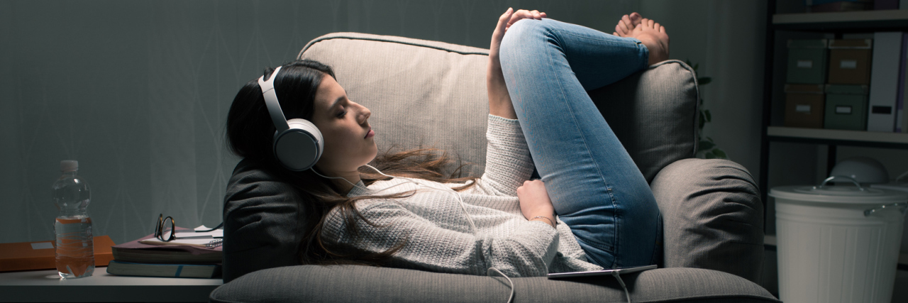 young woman headphones at night curled up on chair