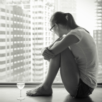 sad woman sitting on windowsill near glass of wine looking out at city black and white
