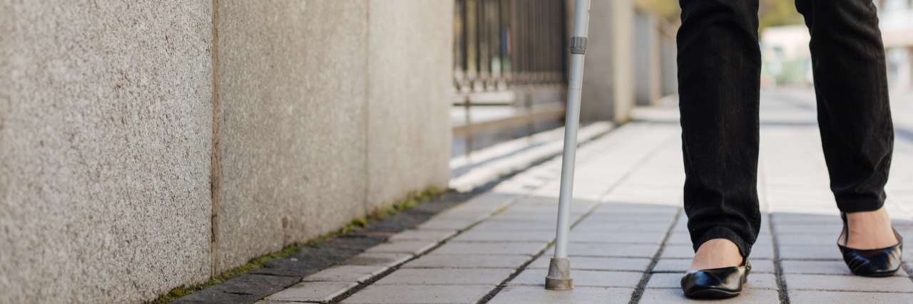 Woman walking along the avenue with crutches.