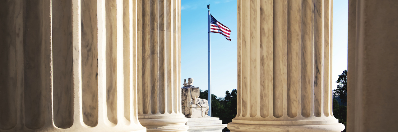The marble columns of the Supreme Court of the United States in Washington DC, with the American flag in the background