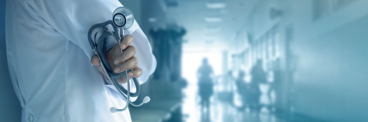 Why Doctors Need to Understand Chronic Illness doctor standing in a hospital corridor holding a stethoscope