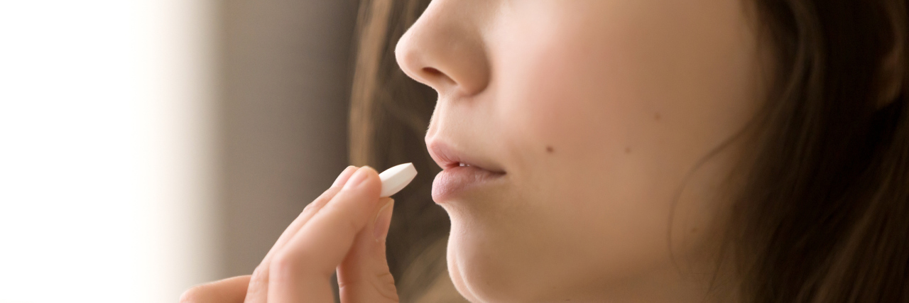 I Need Psychiatric Medication to Feel 'Normal' Close up image of woman putting white round pill in mouth. Sick female taking medicines, antidepressant, painkiller or antibiotic. Young lady drinking contraceptives. Pharmacy and healthcare concept