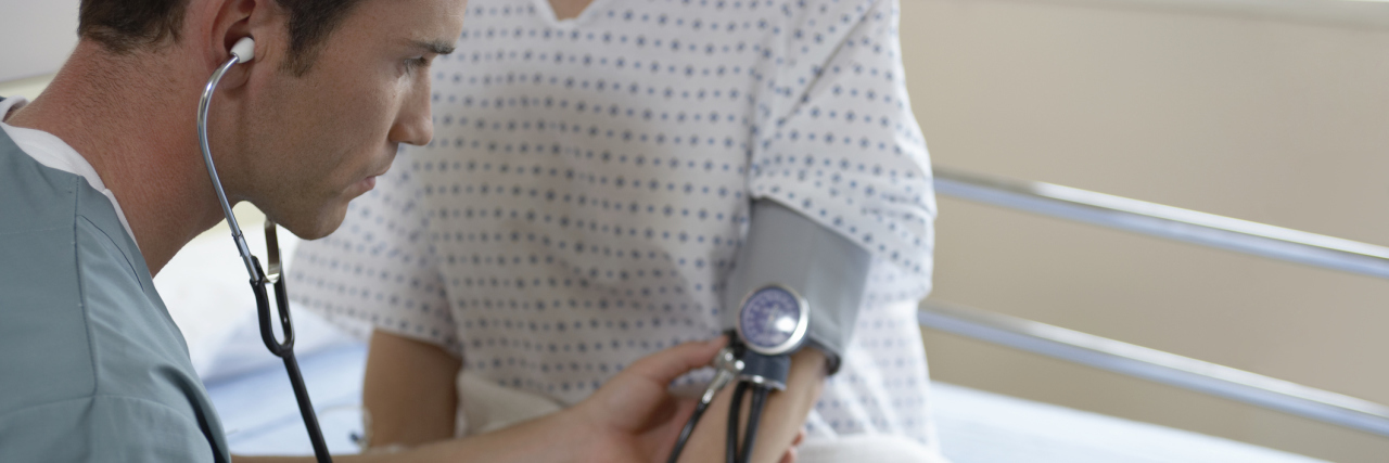 I Received 2 Chronic Illness Diagnoses in One Day A doctor checking a woman's blood pressure at an appointment.
