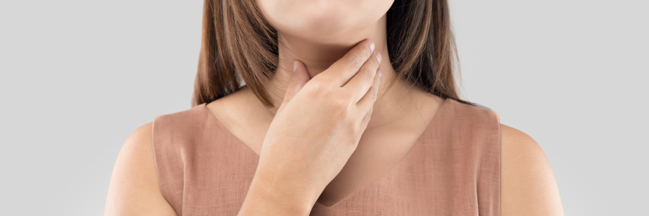 woman with hand to throat against gray background