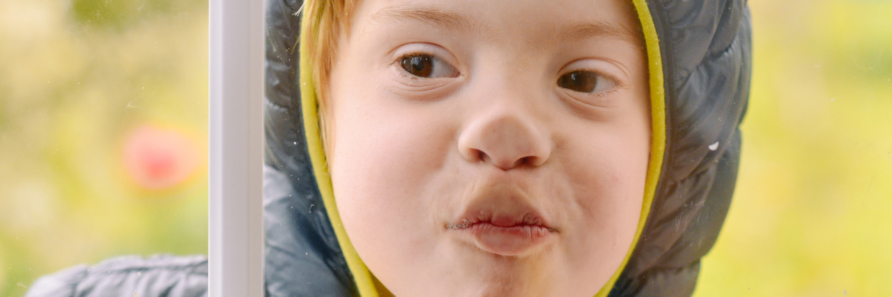 When a Stranger Showed Kindness to My Son With Down Syndrome Boy with Down syndrome smashing his face against a window, he is wearing a hood around his head.