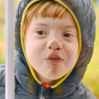 Boy with Down syndrome smashing his face against a window, he is wearing a hood around his head.