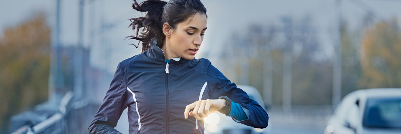 Why I Enjoy Exercising With Chronic Illness woman running and checking her time on her watch