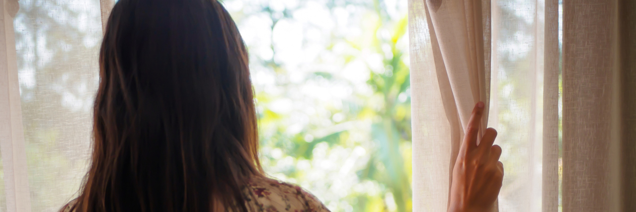 Beating the Depression That Came With My Meniere's Disease Diagnosis woman pulling back a curtain to look out the window