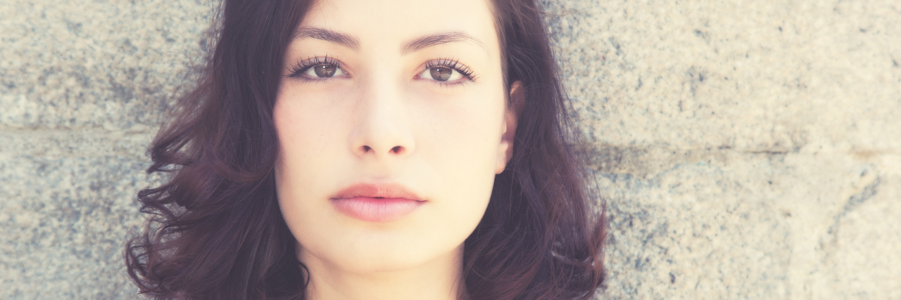 Response to Article About Positive Emotions and Chronic Pain woman with short brown hair standing against a wall and staring at the camera