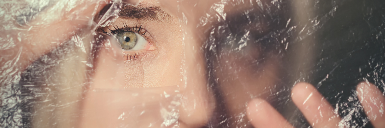 When Your Eating Disorder Makes Your Body Feel Like a Prison Woman looking scared through hole in transparent plastic curtain, scared and alone in dark
