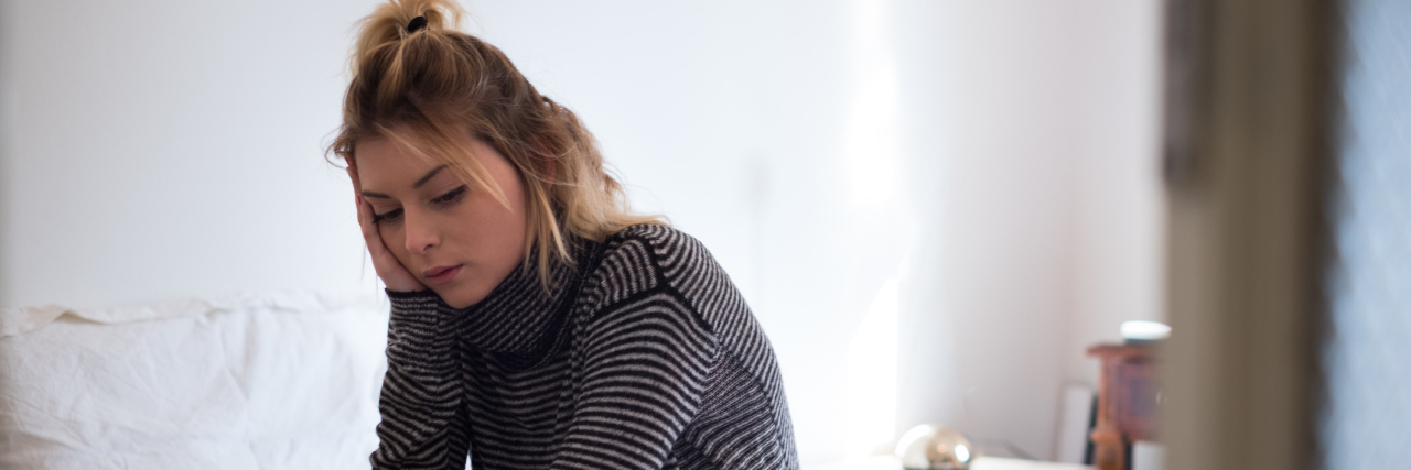 The Importance of Listening to Your Body When You Have Lyme Disease A woman sitting on her bed, with an expression deep in thought.