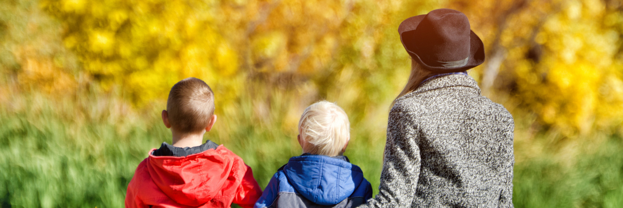 What It's Like to Pass Fabry Disease On to Your Children Mom and two children are sitting on the pier. Sunny autumn. Back view