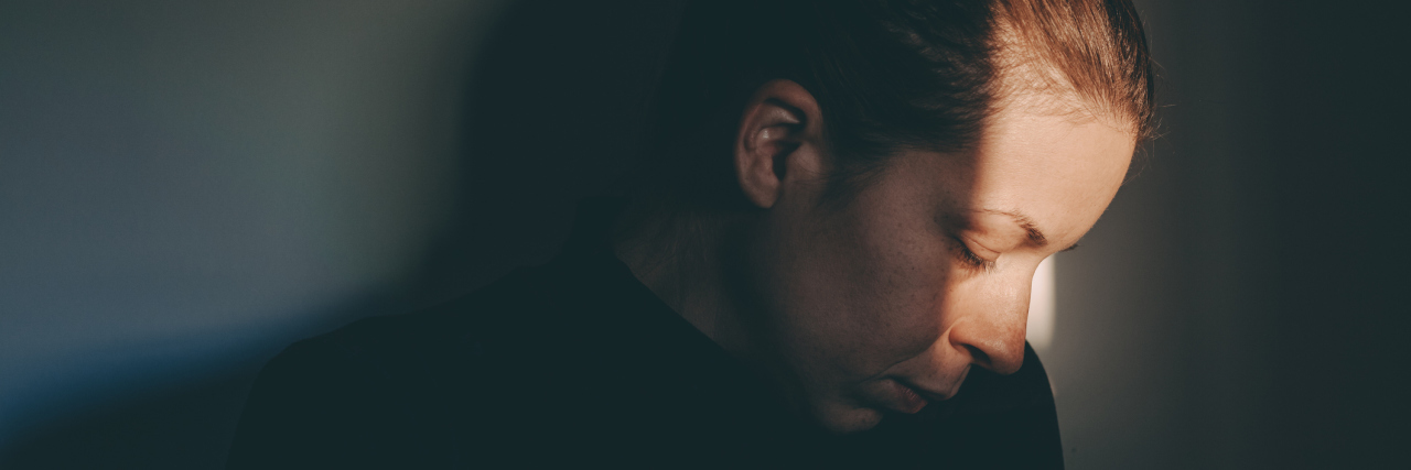 When Illness Keeps Me From My Responsibilities A woman in the shadows, with light hitting part of her face, looking upset.