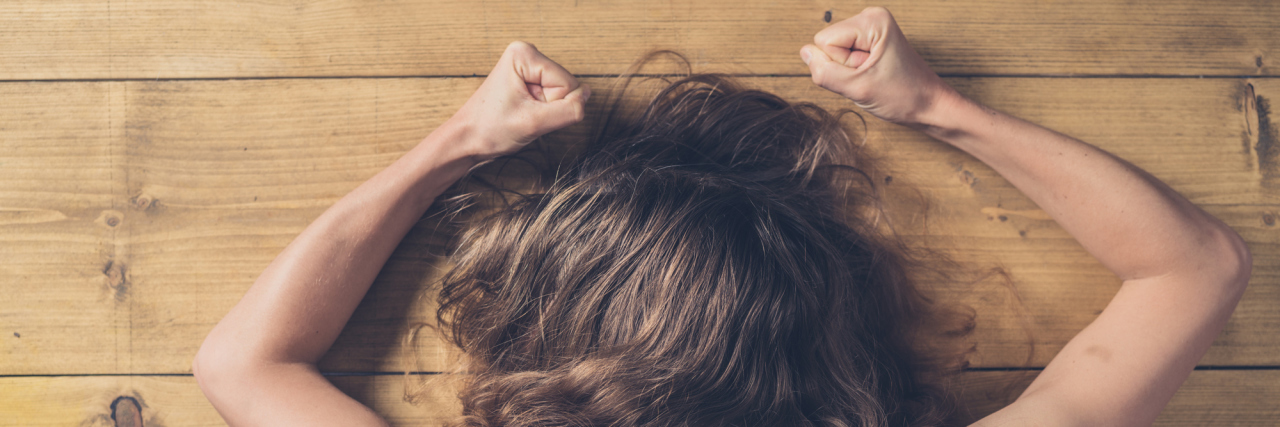 woman with clenched fists lying on wooden table