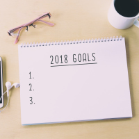 notepad saying "2018 goals" on a table with a pair of glasses and a glass of coffee