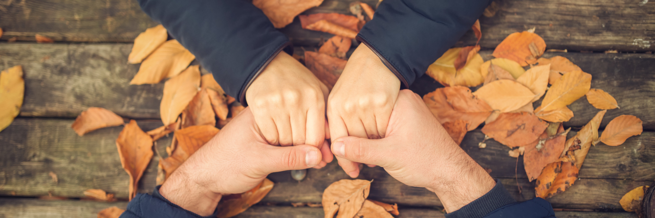 How to Talk to People With an Invisible Illness photo of two hands holding another's on a table with leaves.