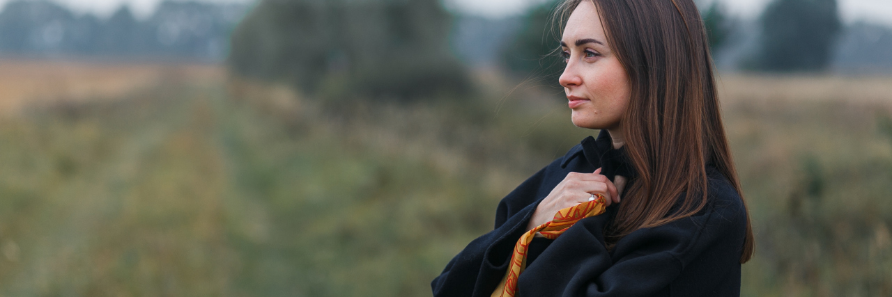 Living 'Patiently Well' With Mixed Connective Tissue Disease woman standing in a field wearing black and holding an orange scarf