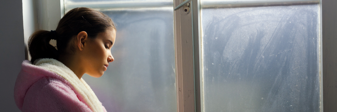 Why New Year's Resolutions Are Damaging to My Mental Health Sad woman standing at a window.