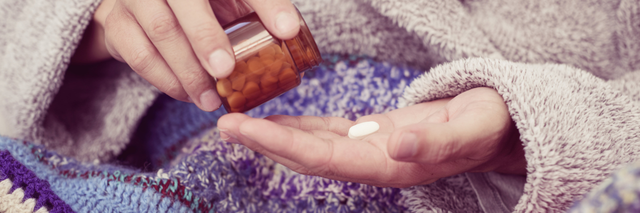 person wrapped in a blanket and pouring a pill from a bottle into their hand