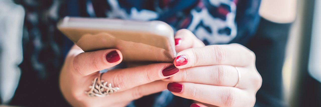A closeup shot of a girl's hands with red nails holding a smartphone